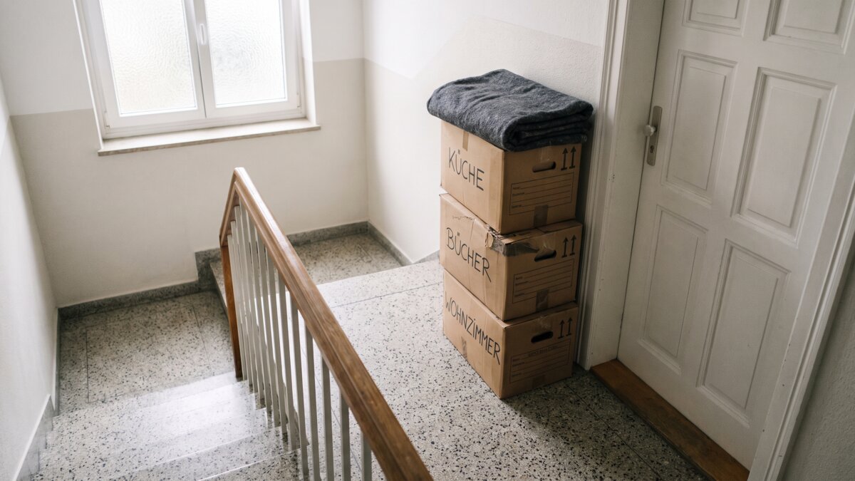 Gestapelte Umzugskartons vor einer Wohnungstür im Treppenhaus