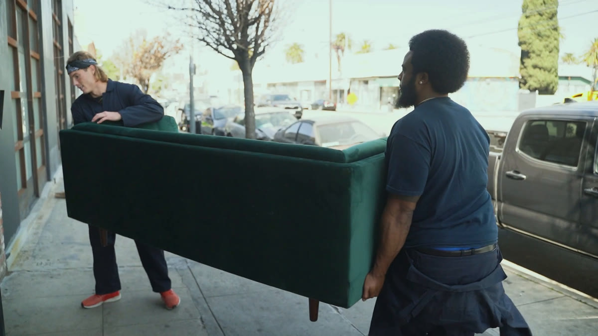 Zwei Möbelpacker tragen gemeinsam ein Sofa über den Gehweg